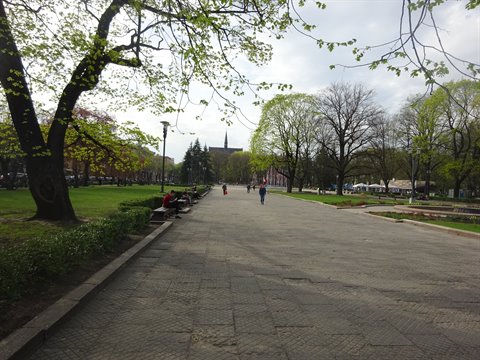 Paved walkway in Sofia's park, leafy trees and strollers under cloudy sky