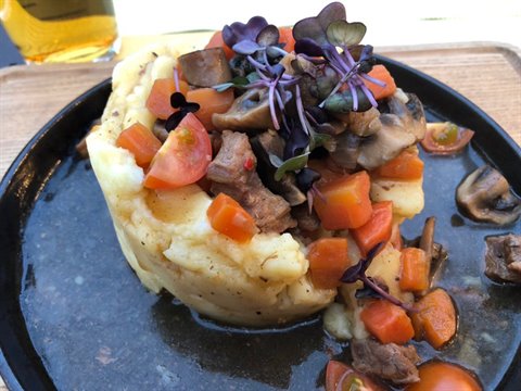 Black plate with mashed potatoes, mushroom and carrot stew, purple microgreens