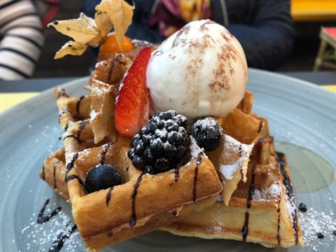 Waffle topped with ice cream, strawberry, berries and chocolate on grey plate