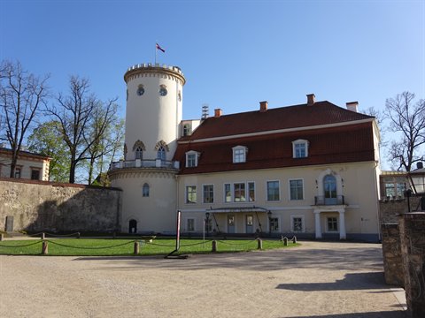White round tower and red-roofed building of Cēsis Castle under blue sky