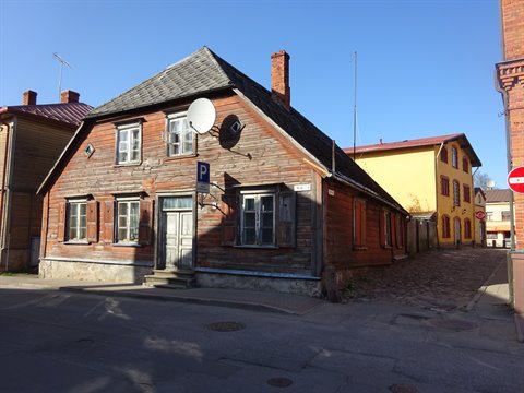 Old red wooden house with shingled roof beside yellow buildings, cobblestone street
