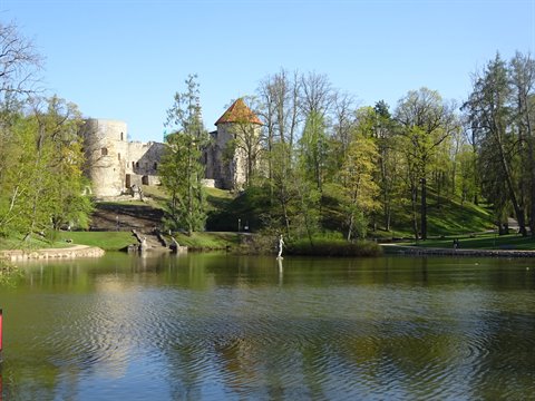 Cēsis stone castle with red-roofed tower reflected in lake among green trees