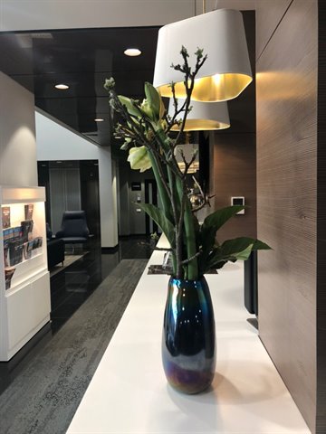 Dark iridescent vase with branches and white flowers on modern lobby counter
