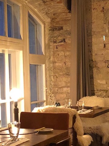 Set tables against exposed brick, lit lamp, sheepskin chairs, evening