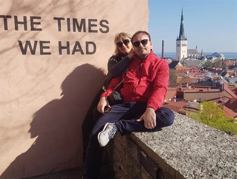 Couple sitting on stone wall beside painted text, Tallinn with Oleviste church spire