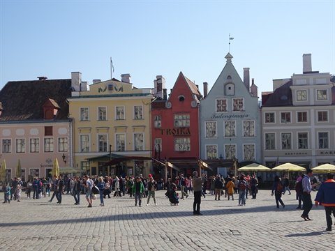 Tourists stroll across Tallinn's Town Hall Square among colorful merchant houses