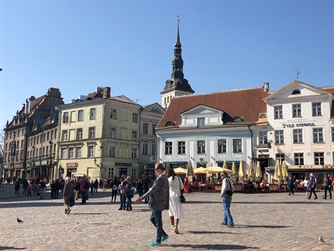 Tourists walk through Tallinn Town Hall Square, colorful buildings and café umbrellas