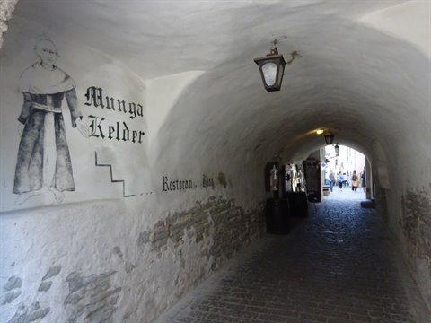 Vaulted stone passage with Munga Kelder sign, monk mural and lantern, Tallinn
