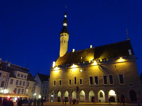 Tallinn Town Hall lit up at night on Raekoja Square, people under the arcades