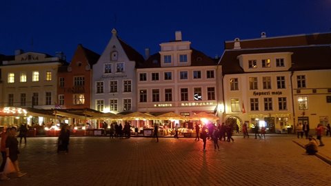 Tallinn Town Hall Square at night, illuminated guild houses and market stalls with visitors