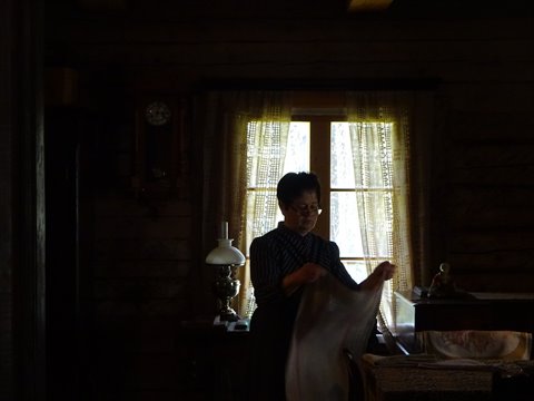 Woman folding cloth by the bright window inside a wooden house