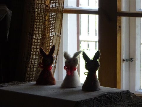 Three felt rabbits with red bows on the table by the window
