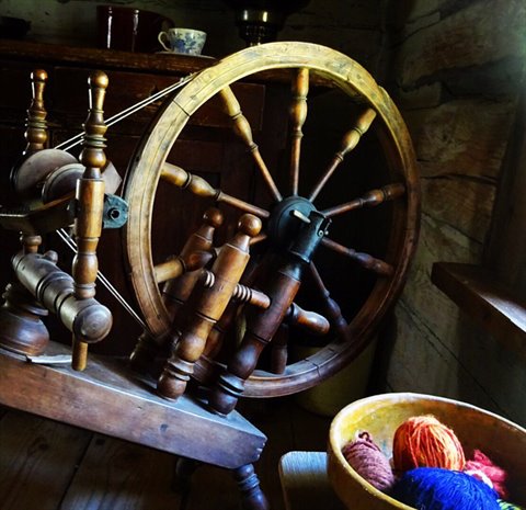Antique wooden spinning wheel with colorful yarn balls in a bowl by the window