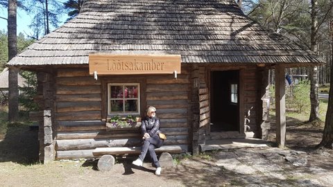 Woman sitting on the bench of an old log cabin, Lōtsakamber sign, open-air museum
