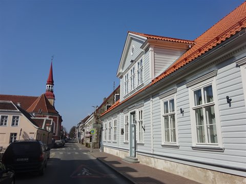 White wooden house with orange tiled roof and church spire, Pärnu