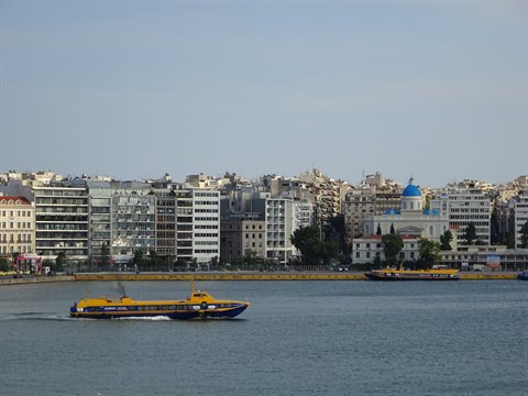 Yellow ferry sailing in Piraeus port, blue-domed church in the background