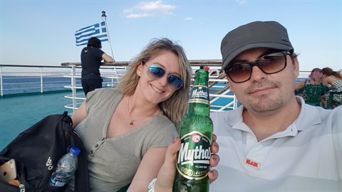 Couple with Mythos beer on a ferry deck, Greek flag waving