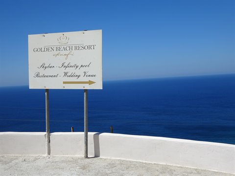 Golden Beach Resort sign with arrow in front of the blue sea