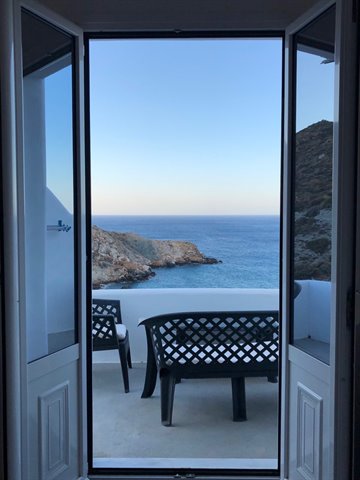 Open door onto terrace with black benches facing rocky coast and blue sea