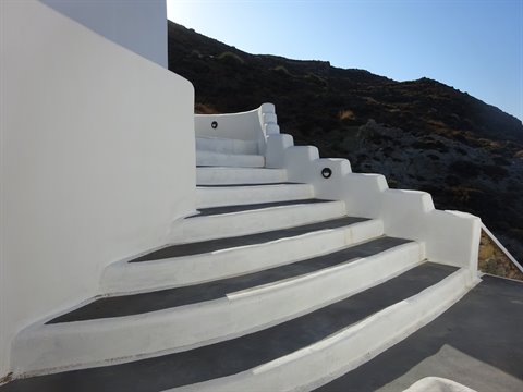 Curved whitewashed staircase climbs toward rocky hill under blue sky