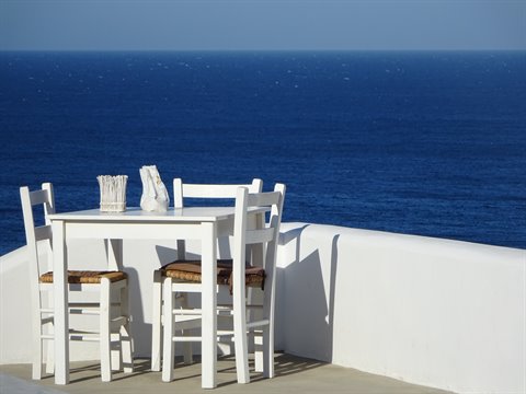 White wooden table and chairs on a terrace above the deep blue sea