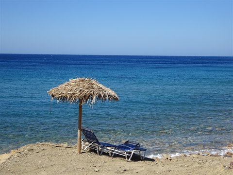 Straw parasol and two empty sunbeds on sandy beach by blue sea