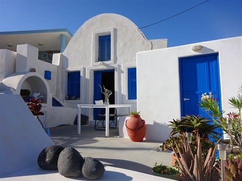 Whitewashed Cycladic house with blue doors, amphorae and succulents under the sun