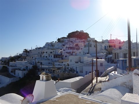 Cycladic hillside village of whitewashed houses under intense sunlight, utility poles in front
