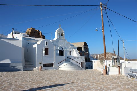 White bell tower church on a stone-paved square, blue sky