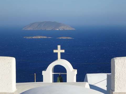White bell tower with cross over the Aegean Sea, volcanic islands beyond