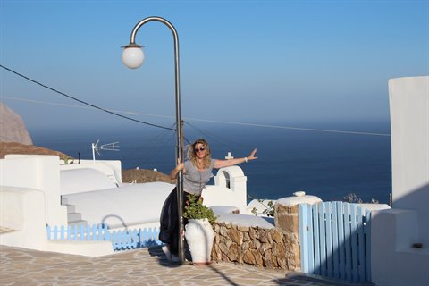 Woman with open arms by a street lamp among white houses and blue gate over the sea