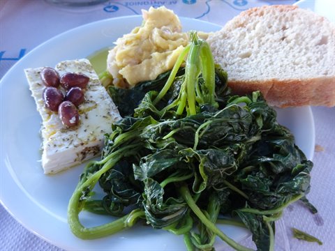 Plate with feta olives boiled greens hummus and bread on tavern table