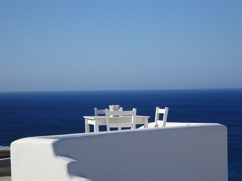 White table and chairs on a plastered terrace facing the deep blue sea