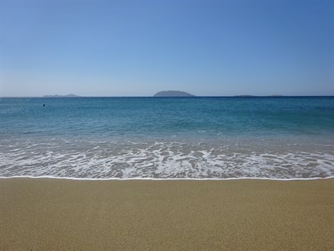 White foamy wave on golden sand, small islets on the blue horizon