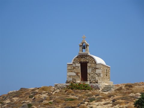Small white stone chapel with bell tower on dry hill under blue sky