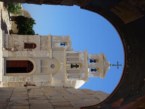 White bell tower with bells and cross framed by a painted arch