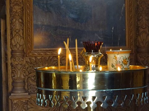 Lit candles on a golden stand before an icon in an Orthodox church