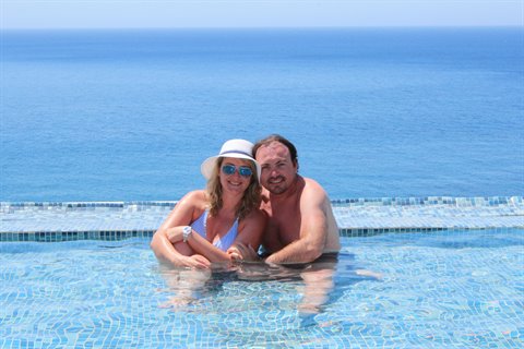 Couple hugging in infinity pool, blue mosaic tiles, open sea behind