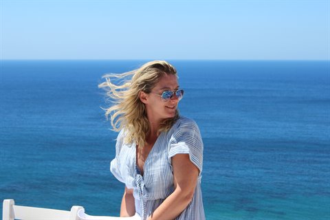 Blonde woman in sunglasses and striped dress by the blue sea
