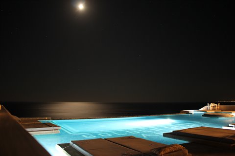 Illuminated pool at night with sun loungers, full moon over dark sea