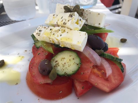 Greek salad with feta, tomatoes, cucumber, olives and capers on white plate