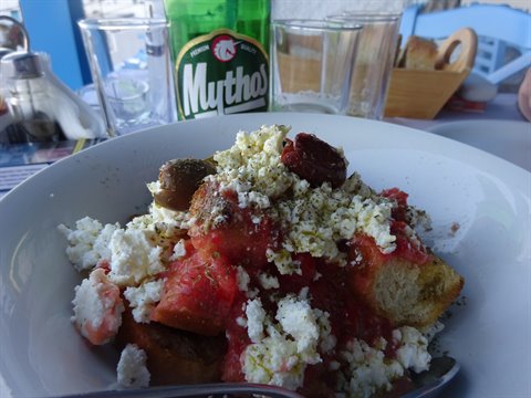 Dakos with feta and tomato in a white bowl, Mythos beer on the taverna table