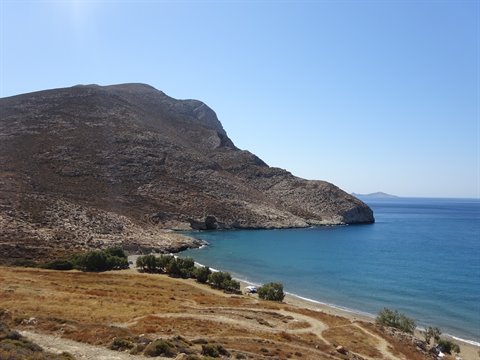 Bay with sandy beach and arid rocky headland above blue sea