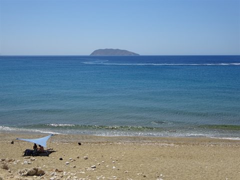 Sandy beach with blue tarp shelter, two people resting, island on the horizon