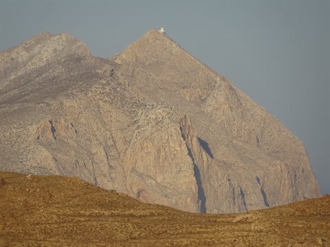 Arid rocky mountain under hazy sky, white building on the summit