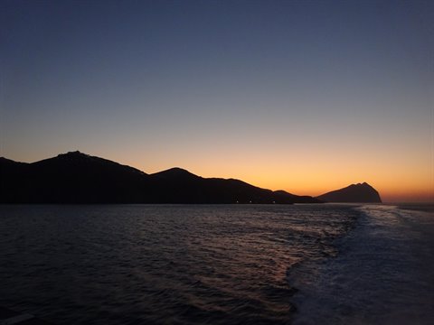 Dark coastline at dusk seen from a boat, white wake on the water