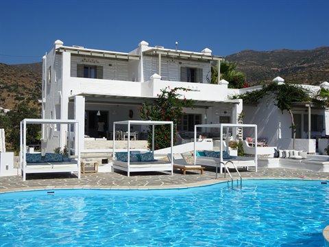 Blue pool with white canopy daybeds in front of a Cycladic hotel