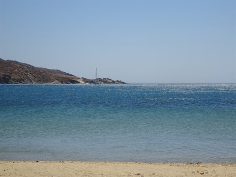 Turquoise waters by a sandy beach, sails and dry cliffs under blue sky