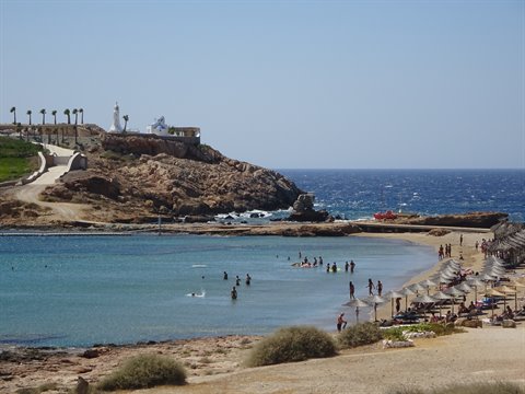 Swimmers on sandy beach with umbrellas, rocky headland and white chapel