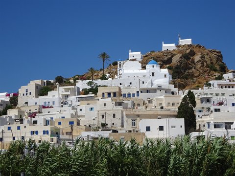 Cycladic village with whitewashed houses and blue-domed church beneath brown rocks